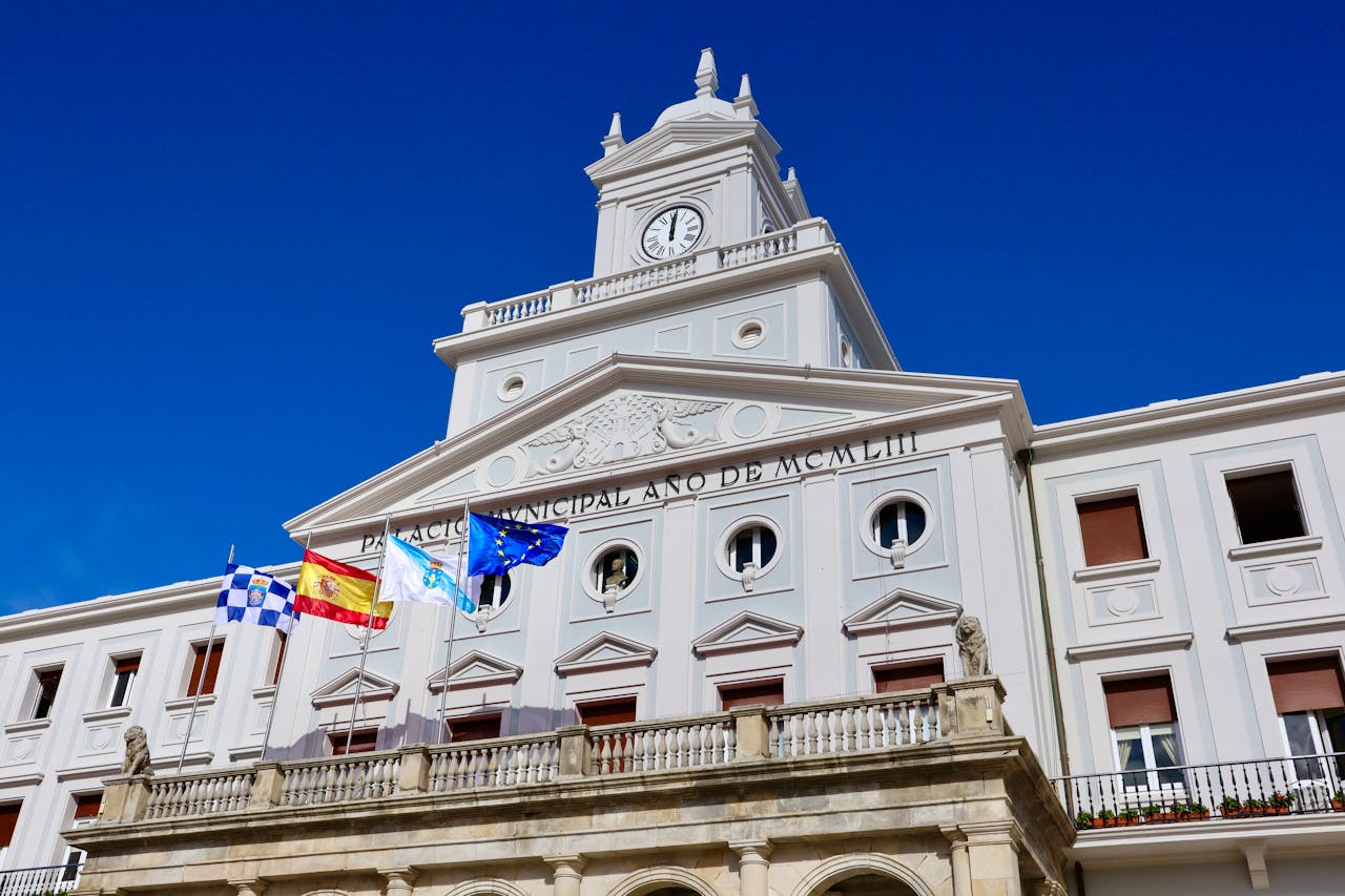 services-img Low-angle view of the Municipal Palace with flags in Ferrol, Spain on a sunny day.